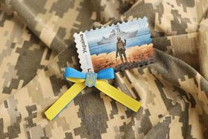 TERNOPIL, UKRAINE - SEPTEMBER 2, 2022 Famous Ukrainian postmark with russian warship and ukrainian soldier as wooden souvenir on army camouflage uniform photo