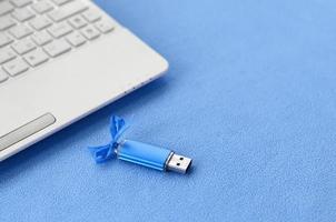 la tarjeta de memoria flash usb azul brillante con un lazo azul se encuentra sobre una manta de tela polar azul claro suave y peluda junto a una computadora portátil blanca. diseño clásico de regalo femenino para una tarjeta de memoria foto