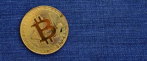 Golden Bitcoin lies on a blue jeans fabric. New virtual money. New crypto currency in the form of the coins photo