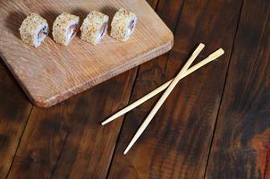 A detailed shot of a set of Japanese sushi rolls and a device for their use chopsticks , which are located on a wooden cutting board on a table in the kitchen of a sushi bar photo