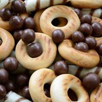 A lot of crispy sweet tubules, chocolate melting balls and yellow bagels lie on a wooden surface. Close up view photo