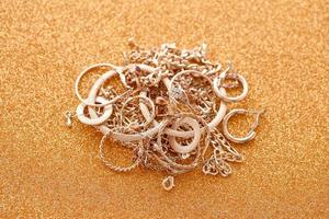 Many expensive golden jewerly rings, earrings and necklaces on golden glitter background with shiny sparkles. Pawn shop or jewerly trading photo