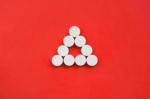 Several white tablets lie on a bright red background in the form of an even triangle. Background image on medicine and pharmaceutical topics photo