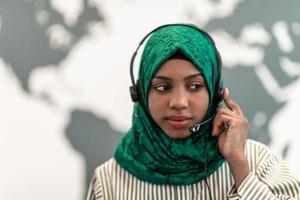 Afro Muslim female with green hijab scarf customer representative business woman with phone headset helping and supporting online with customer in modern call centre photo