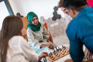 Multiethnic group of business people playing chess while having a break in relaxation area at modern startup office. Selective focus photo