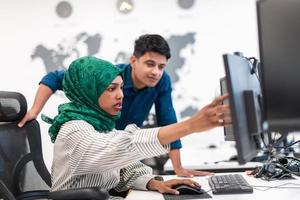 Multiethnic startup business team Arabian woman wearing a hijab on meeting in modern open plan office interior brainstorming, working on laptop and desktop computer. Selective focus photo