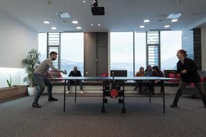 un joven hombre y una mujer de negocios que empiezan a jugar tenis de mesa en un espacio de oficina creativo moderno grupo de personas que se reúnen y hacen una lluvia de ideas en segundo plano foto