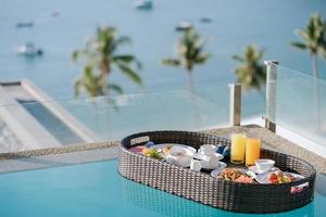 Breakfast set in tray in swimming pool, floating breakfast in tropical resort villa with ocean view. photo