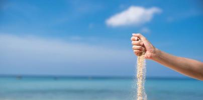 Woman pouring the sand from hand on the beach, blue sky. photo