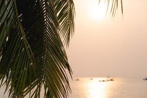 puesta de sol sobre el mar con palmeras de coco en la playa tropical y cielo naranja pastel. foto