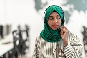 mujer musulmana con pañuelo verde hiyab representante del cliente mujer de negocios con auriculares de teléfono ayudando y apoyando en línea con el cliente en un centro de llamadas moderno