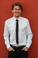 Portrait of startup businessman in a white shirt with a black tie standing in front of red wall outside photo