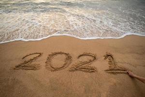 Handwriting year 2021 on sand and foam wave on beach. photo