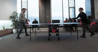 un joven hombre y una mujer de negocios que empiezan a jugar tenis de mesa en un espacio de oficina creativo moderno grupo de personas que se reúnen y hacen una lluvia de ideas en segundo plano foto