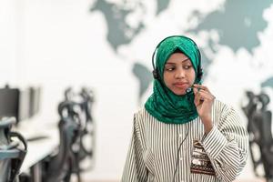 Afro Muslim female with green hijab scarf customer representative business woman with phone headset helping and supporting online with customer in modern call centre photo