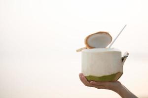 Hand holding fresh coconut on the beach, romantic sunset moment. summer vacation. photo