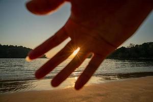 mano del hombre al frente para detener la cámara. vista al mar al atardecer. sol sobre el mar en el cielo naranja. foto