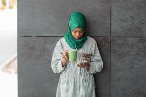 African Muslim businesswoman with green hijab using mobile phone during coffee break from work outside photo