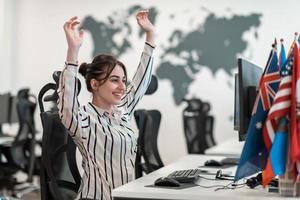 Happy casual business woman celebrating success while working on desktop computer in modern open plan startup office interior photo