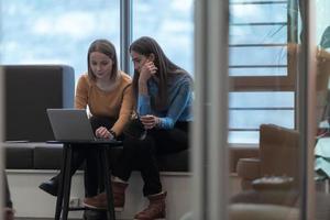 Two business women sitingt in a modern coworking space on a break from work and relax using a laptop. Selective focus photo