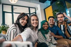 Group of business people during break from the work taking selfie picture while enjoying free time in relaxation area at modern open plan startup office. Selective focus photo