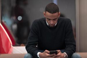 Young African American work in coworking space using smartphone analyzing online market trends, focused man worker reading financial news or browsing internet on phone. Technology concept photo