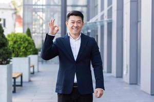 hombre de negocios vendedor asiático en traje de negocios sonríe y muestra su mano todo bien foto