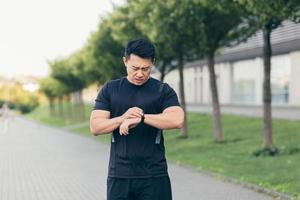 atleta asiático masculino, cansado después de un trote matutino, corre en el parque cerca del estadio foto