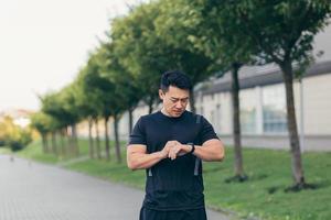 atleta asiático masculino, cansado después de un trote matutino, corre en el parque cerca del estadio foto