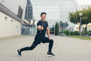 hombre atleta asiático haciendo fitness sonriendo y mirando a la cámara sosteniendo extendido foto