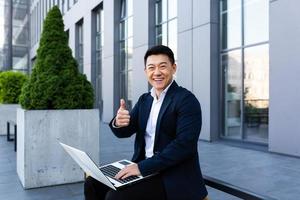 cheerful male asian businessman working on laptop online banking on computer photo