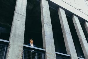 joven empresario asiático de pie cerca de un moderno edificio de oficinas negro hecho de hormigón foto