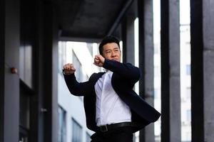 Happy and cheerful Asian businessman dancing near the office rejoices in victory and success photo