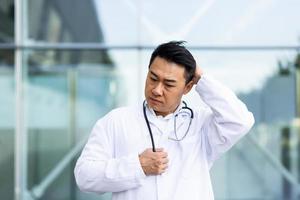 el médico asiático está cansado después del trabajo, deprimido y decepcionado con el trabajo realizado en la calle foto