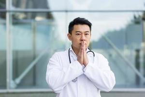 portrait Asian doctor tired after work, puts his hands to his face hoping for a good result photo