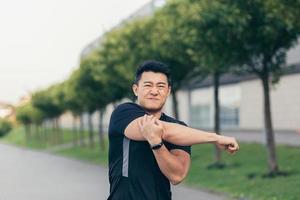Male asian athlete, kneading shoulder pain, sore arm muscles in the park photo