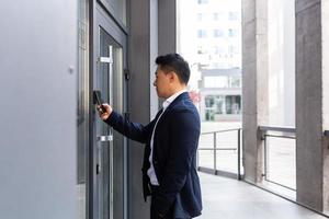 exitoso hombre de negocios asiático abre la puerta del centro de oficinas usando un teléfono inteligente foto