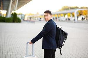 Successful asian businessman near airport and bus station goes with suitcases serious photo