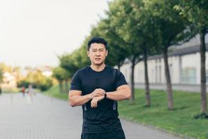 atleta asiático masculino, cansado después de un trote matutino, corre en el parque cerca del estadio foto