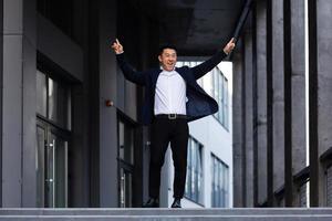 Happy and cheerful Asian businessman dancing near the office rejoices in victory and success photo