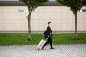 Successful asian businessman near airport and bus station goes with suitcases serious photo