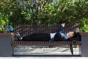 Male Asian businessman lying on a bench and resting after work uses a mobile phone photo