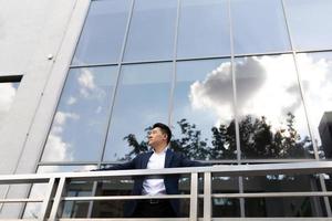 Asian businessman boss stands near his office center on the balcony in a dark color business suit photo