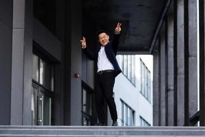 Happy and cheerful Asian businessman dancing near the office rejoices in victory and success photo