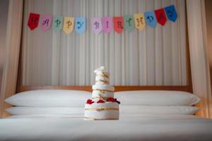 celebrando cumpleaños, sorpresa en la cama con pancarta de feliz cumpleaños y pastel de toallas. foto