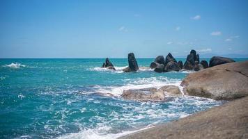 playa rocosa con olas blancas, vistas al océano azul profundo y cielo azul. foto