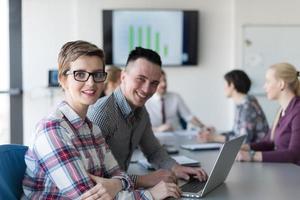 joven pareja de negocios trabajando en laptop, grupo de empresarios en reunión en segundo plano foto