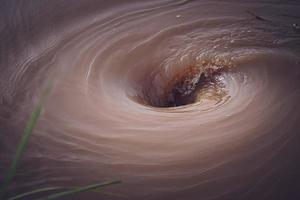 se crea un poderoso vórtice en la superficie verde del río que fluye vigorosamente por las lluvias torrenciales y las inundaciones. foto