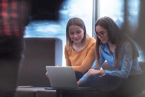 Two business women sitingt in a modern coworking space on a break from work and relax using a laptop. Selective focus photo