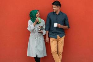 Multiethnic group of casual business people using smartphone during coffee break from work in front of red wall outside photo